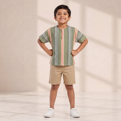 Child wearing a striped shirt and shorts standing against a plain background