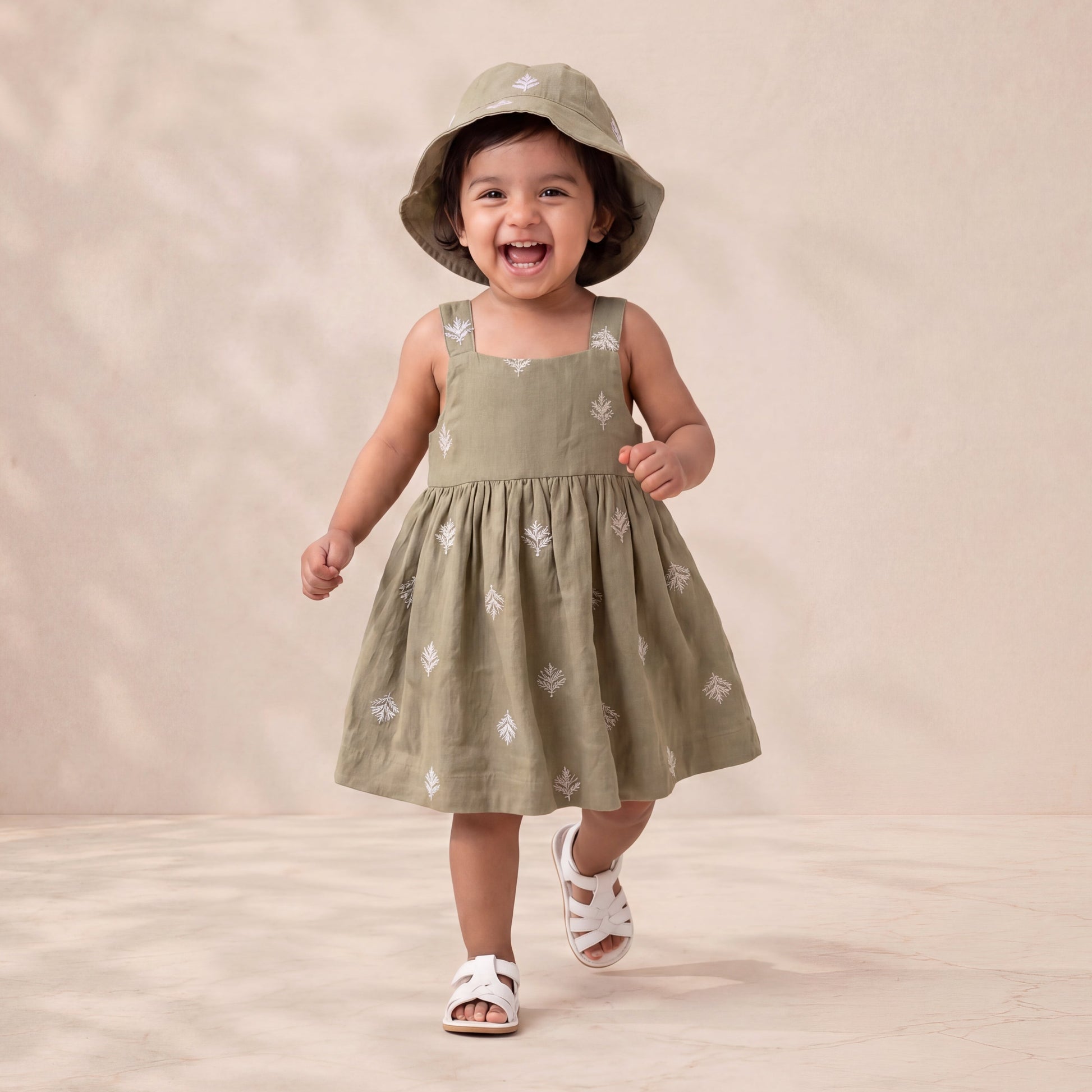 Child wearing a green dress and hat on a beige background
