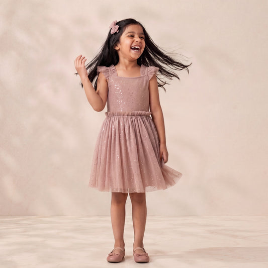 Young girl in a pink dress standing against a plain background