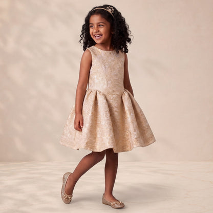 Young girl in a beige floral dress standing against a plain background