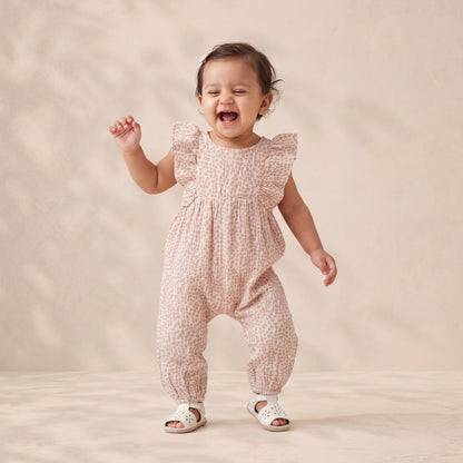 Baby in a pink patterned romper standing on a beige background