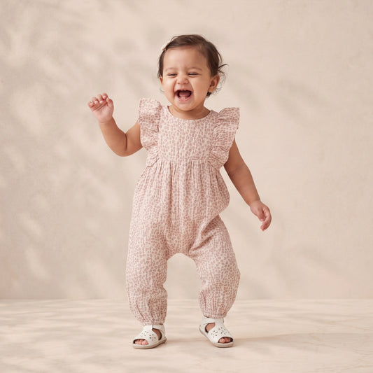 Baby in a pink patterned romper standing on a beige background