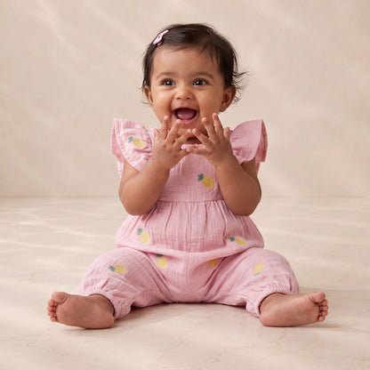 Baby in a pink outfit sitting on a beige surface with a neutral background