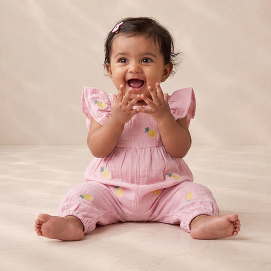 Baby in a pink outfit sitting on a beige surface with a neutral background