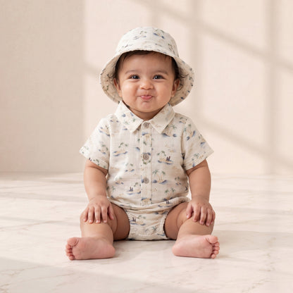 Baby sitting on a light surface wearing a patterned hat and shirt.