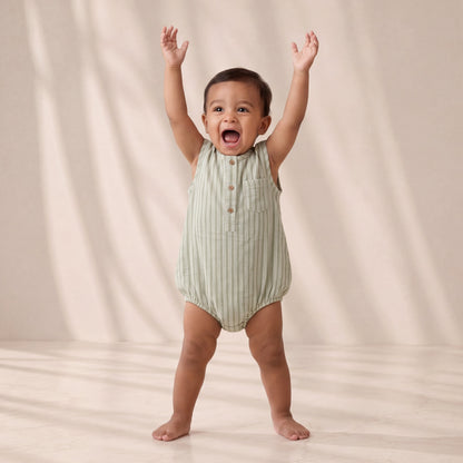 Child wearing a green striped romper with arms raised against a beige background