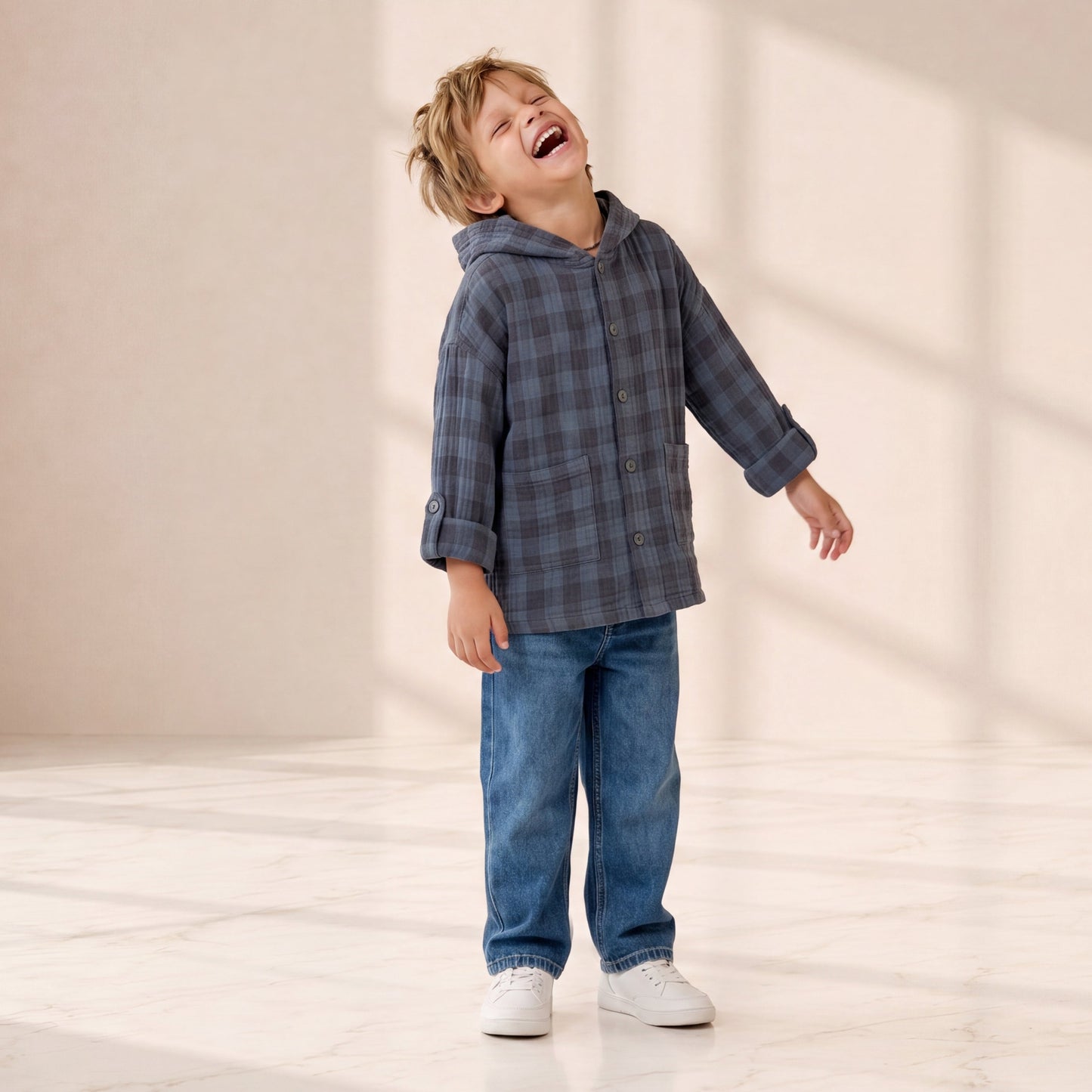 Child wearing a plaid jacket and jeans standing on a reflective surface with a neutral background
