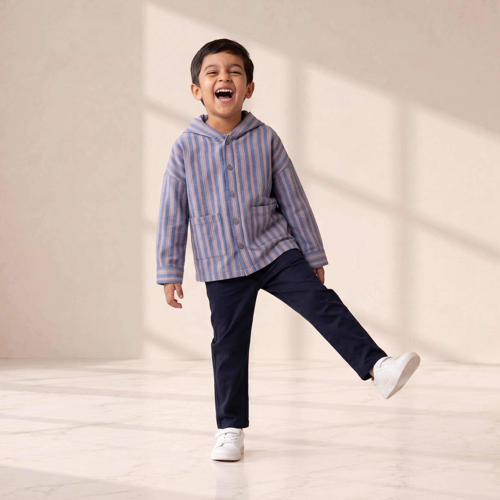 Child wearing a striped hoodie and dark pants, standing in a well-lit room with a neutral background.