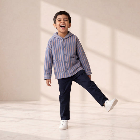 Child wearing a striped hoodie and dark pants, standing in a well-lit room with a neutral background.