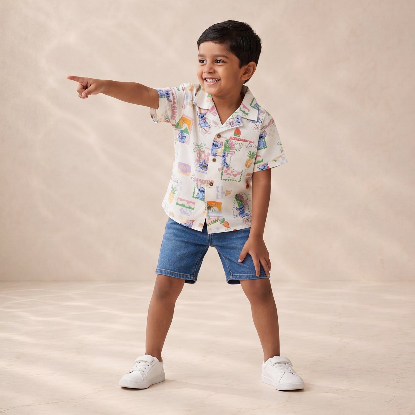 Child wearing a colorful shirt and denim shorts pointing to the side on a beige background