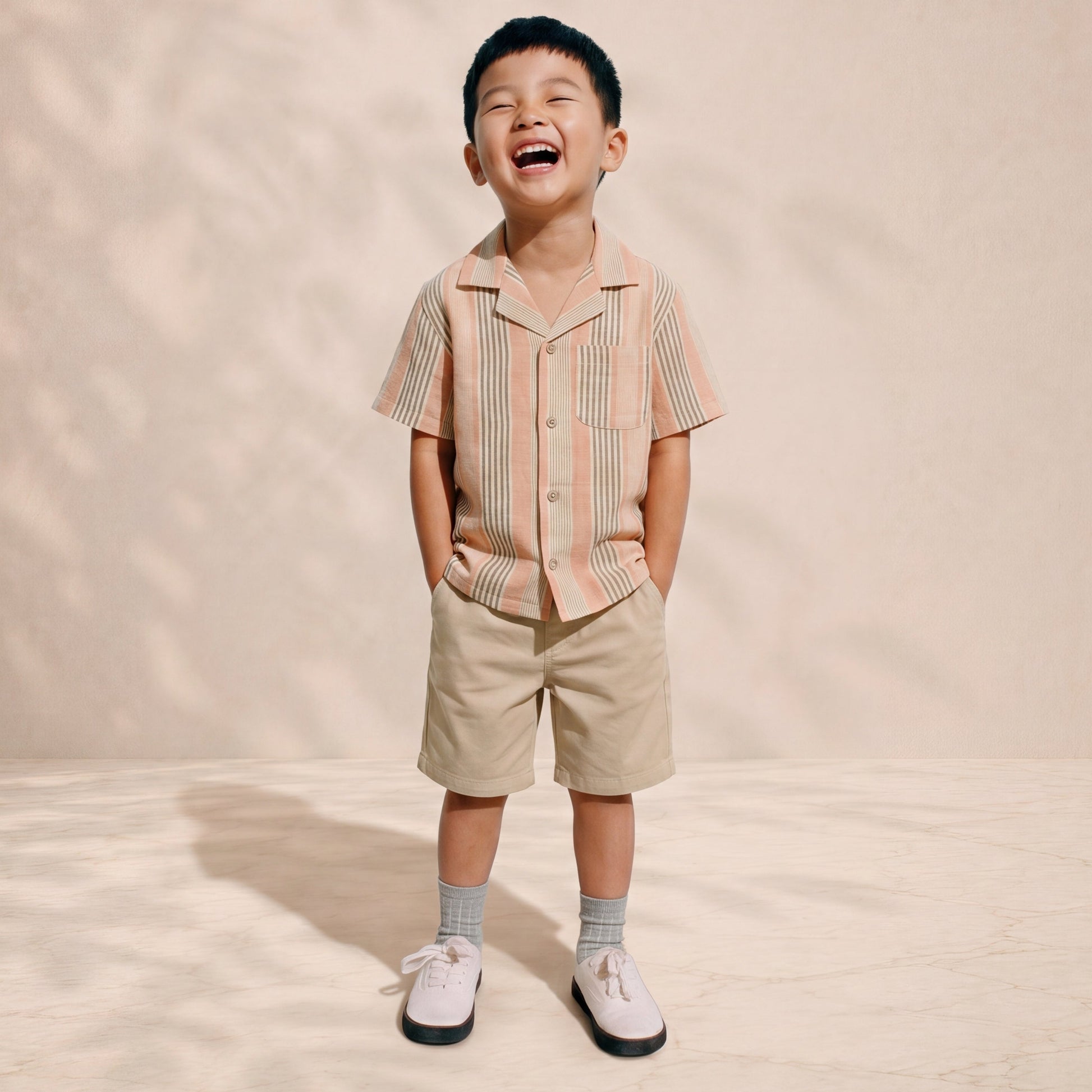 Child wearing a striped shirt and shorts standing on a beige background