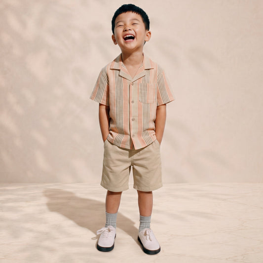 Child wearing a striped shirt and shorts standing on a beige background