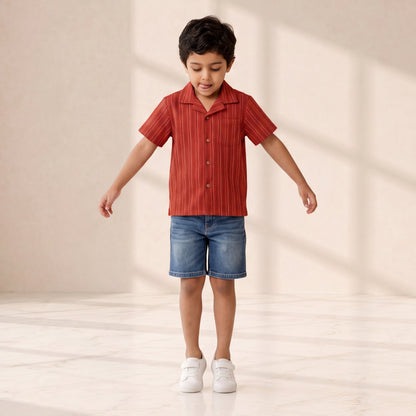 Child wearing a red striped shirt and blue shorts standing on a light wooden floor with a neutral background