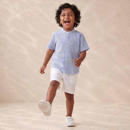 Child wearing a blue striped shirt and white shorts running on a beige background