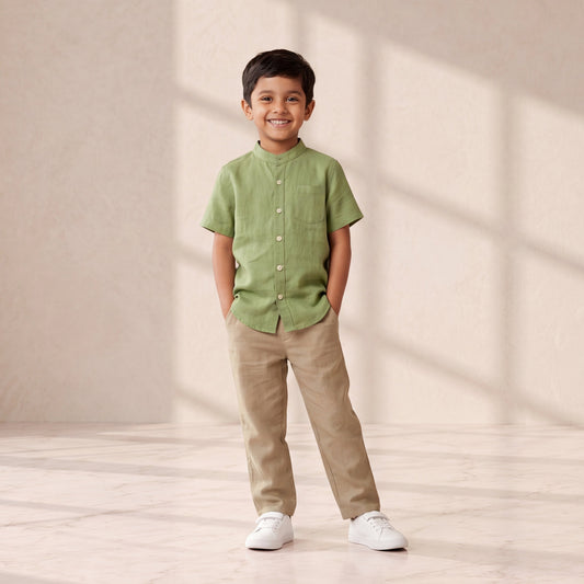Child wearing a green shirt and beige pants standing in a softly lit room.