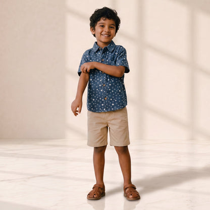 Child wearing a blue patterned shirt and beige shorts standing on a light background