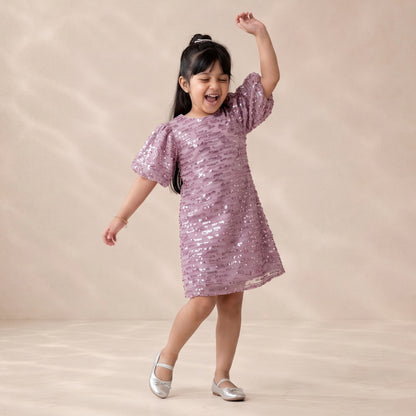 Young girl in a pink sequin dress posing against a beige background