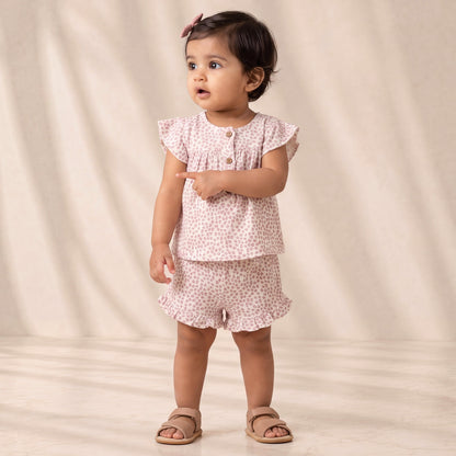 Young child wearing a pink floral outfit standing against a plain background
