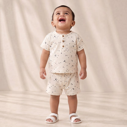 Child wearing a white outfit with small patterns on a plain background