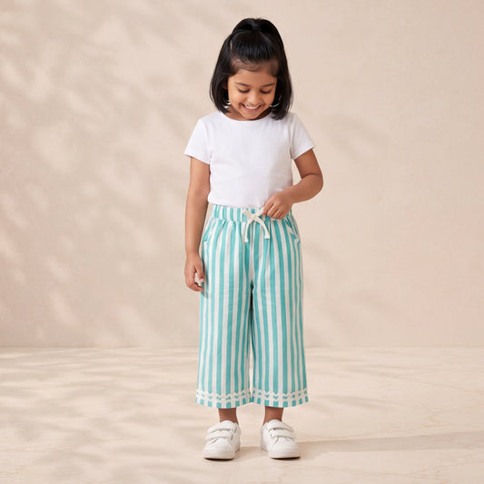 Young girl wearing a white t-shirt and blue striped pants standing on a beige background