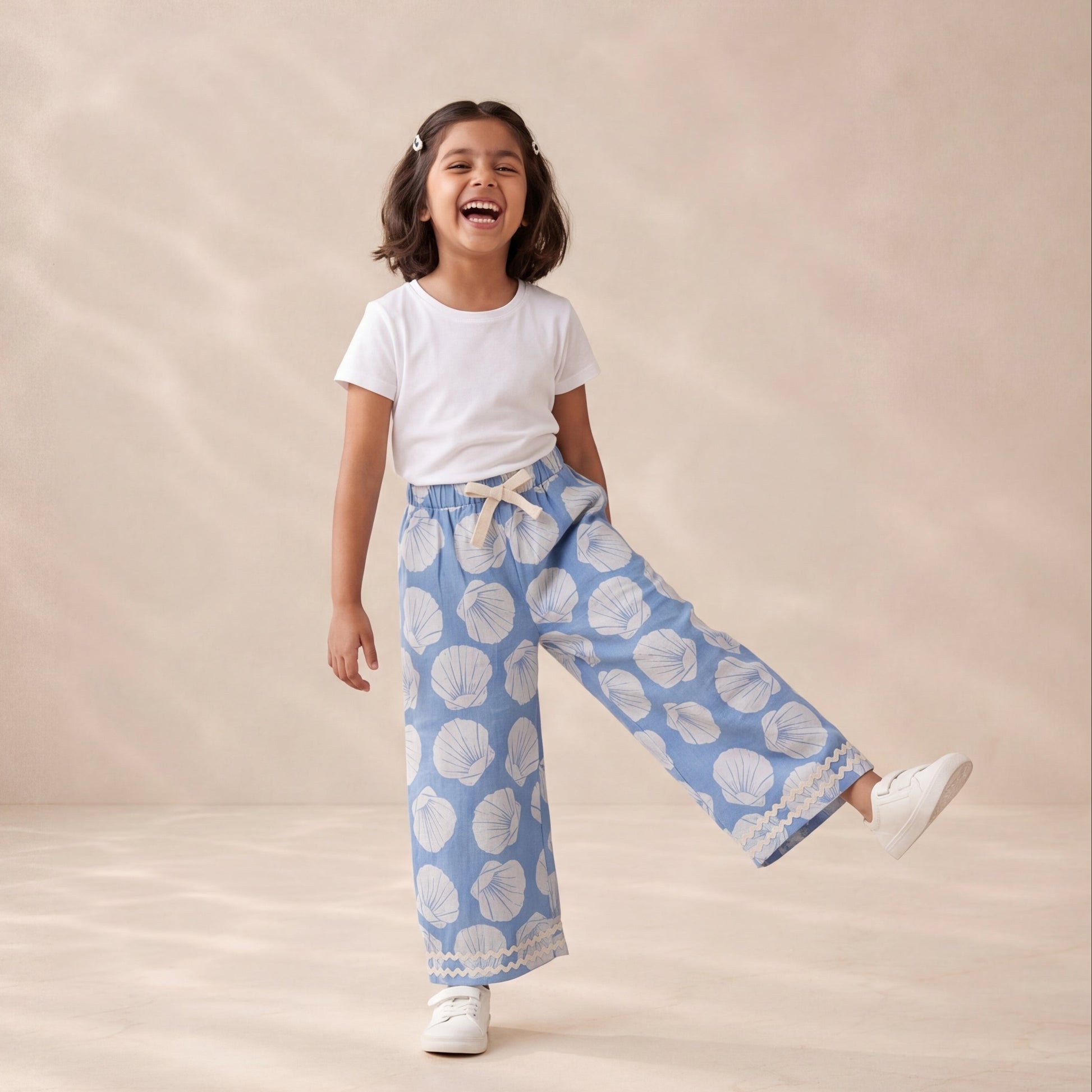 Young girl wearing a white t-shirt and blue patterned pants on a beige background