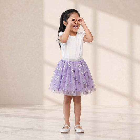 Young girl in a white top and purple skirt standing in a softly lit room.