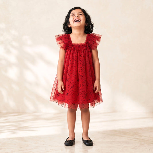Young girl in a red dress standing on a light wooden floor with a neutral background