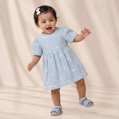 Baby in a light blue dress standing on a beige background