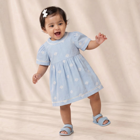 Baby in a light blue dress standing on a beige background