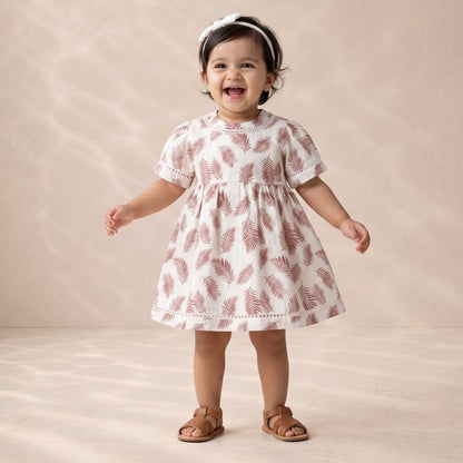 Child wearing a white dress with red patterns on a beige background