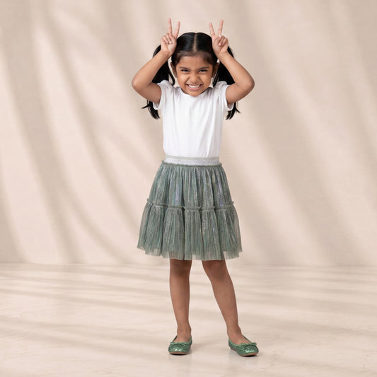 Young girl in a white top and green skirt standing against a beige background