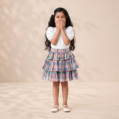 Young girl in a plaid skirt and white top standing against a beige background